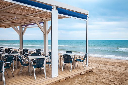 Sea side bar interior with wooden floor and metal armchairs on the sandy beach