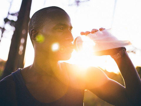Afro-american athlete drinking water close up shot with lens flare in late afternoon in the woods