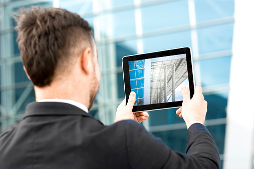 Businessman taking photo of contemporary building with digital tablet