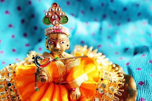 Hindu God Lord Krishna Brass idol of baby lord Krishna, a Hindu god, dressed in bright yellow clothing, against a polka dotted aqua colored cloth background, sporting his legendary musical flute. Ideal for Hindu religious use and festivals - like Janamashtami, Gokul ashtami. mahabharata stock pictures, royalty-free photos & images