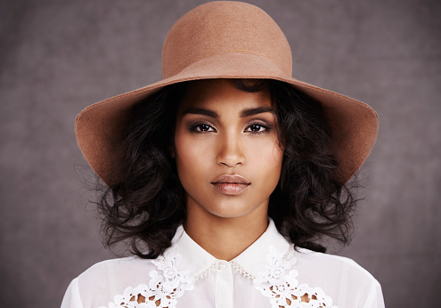 Cropped portrait of a stylish young woman wearing a hat standing against a gray background