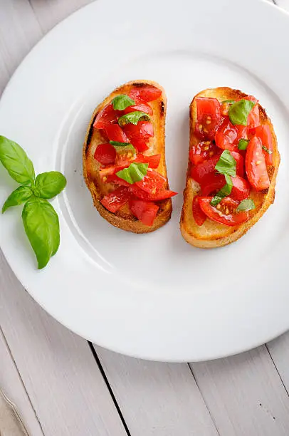 Bruschetta with sliced tomatoes and basil on white plate