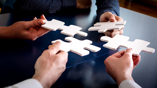 A close-up of four business people holding pieces of a puzzle.