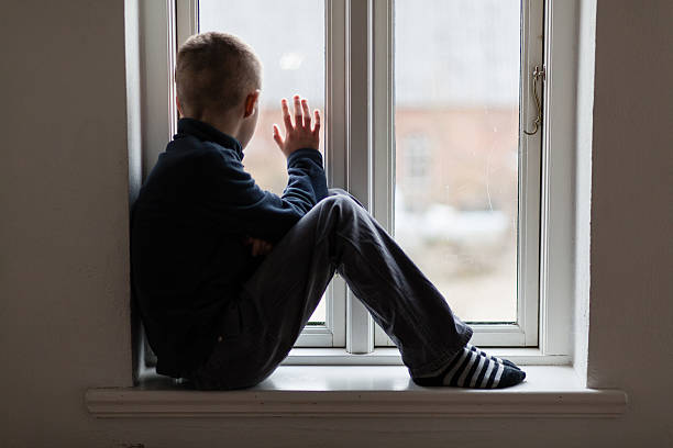 istock Young boy sitting on a windowsill waving 517895264