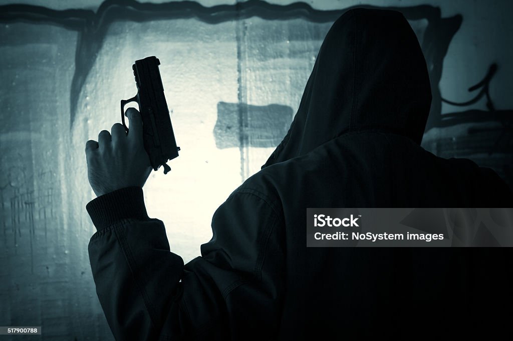 Silhouetted man with gun Silhouetted man with gun against underground wall background Handgun Stock Photo