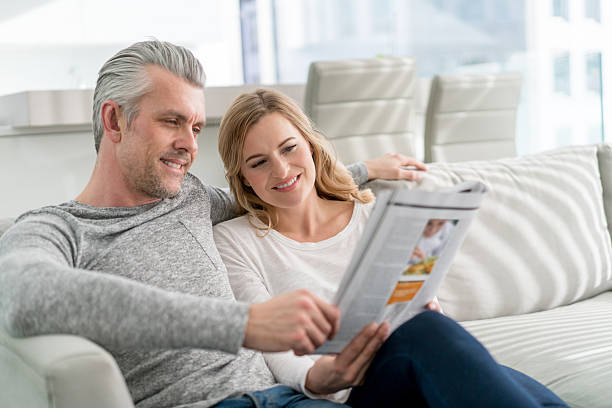 couple at home reading a magazine - for rent sign house sign happiness imagens e fotografias de stock