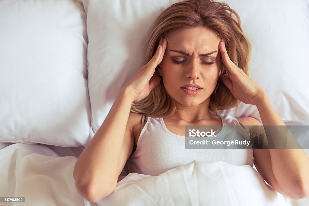 Girl in the morning Top view of tired beautiful girl keeping hands on her temples while lying in bed Adult Stock Photo