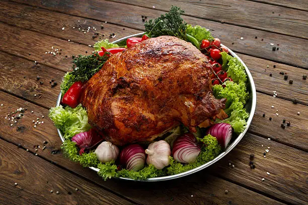 Restaurant food, roasted pork shoulder. Meat dish. Festive banquet dish, holiday dish. Catering. Served main dish, roasted pork with vegetables and herbs. Plate at wooden rustic background.