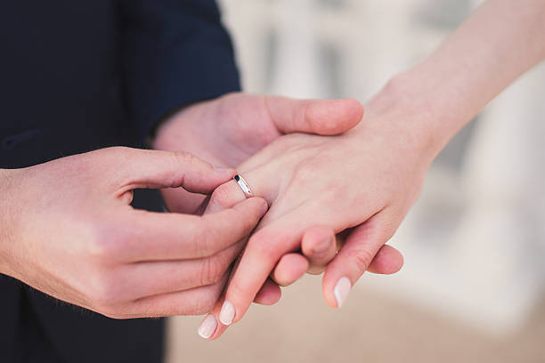 istock groom putting a wedding ring onto the bride's finger 517904820