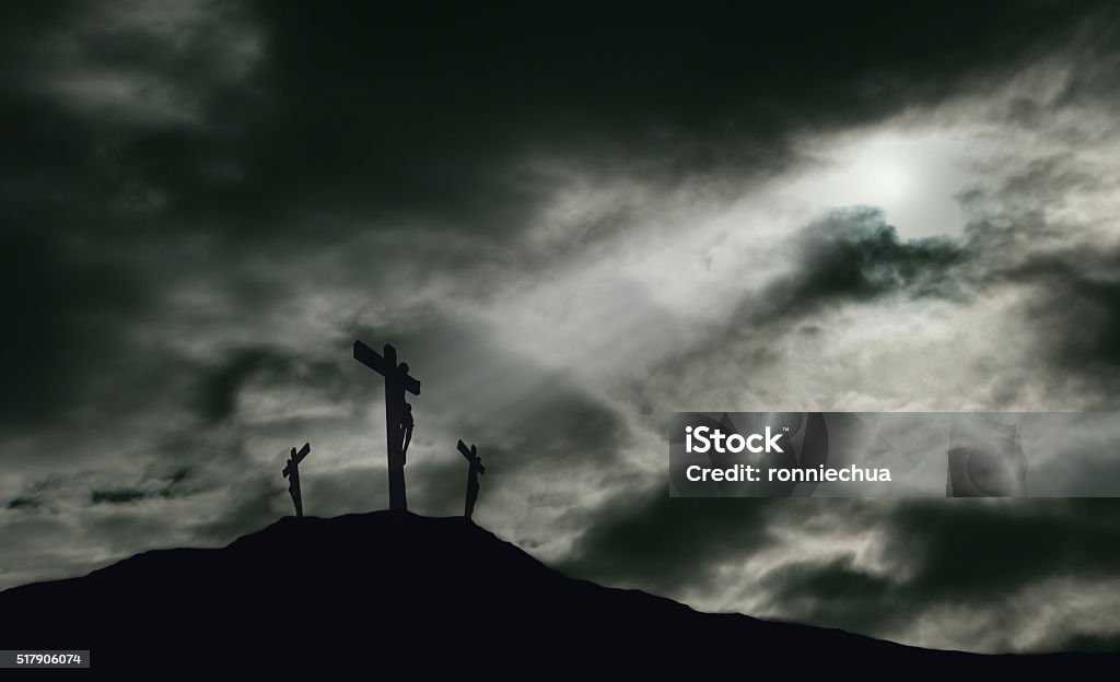 Crucifixion of Jesus on Golgotha With Copy Space A depiction of the crucifixion of Jesus Christ on a cross with 2 other robbers nearby on Calvary. The sky is darkened with rays of light breaking through the clouds onto the cross for drama. Concept of the death of Jesus on Good Friday and His resurrection on Easter Sunday. Horizontal orientation with copy space. Good Friday Stock Photo