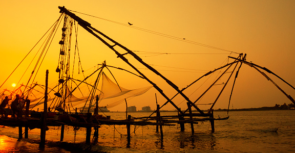 Kochi, Kerala, India - March 19, 2015. A group of fishermen hauling in a Chinese fishing net at sunset in Kochi, India.
