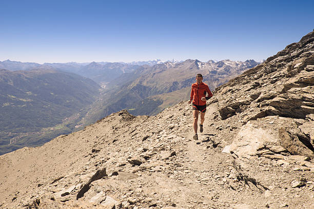Trail running on the mountains A man running up on a hill under a blue sky strada sterrata stock pictures, royalty-free photos & images