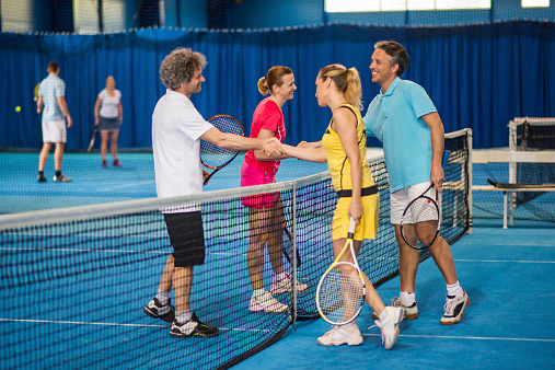 Two couples shaking hands after a tennis match.