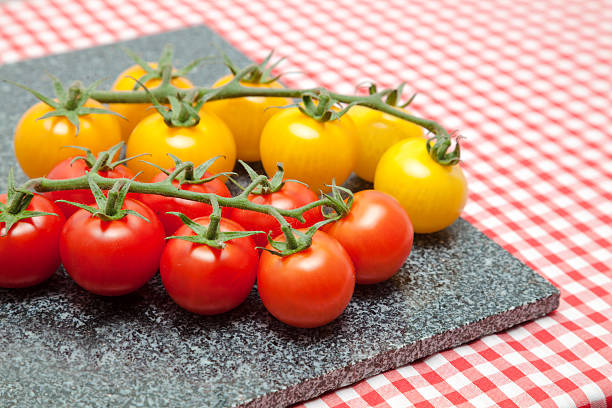 rosso and amber tomatoes - red and yellow cherry  tomatoes on granite chopping board on red gingham tablecloth