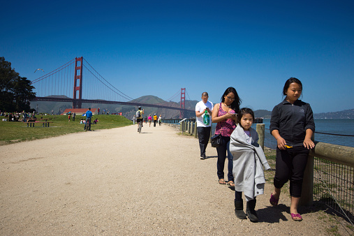San Francisco, USA - April 13, 2014: View on a spring day of the San Francisco harbour Golden Gate Bridge with an Asian family in the foreground and walkers and a polarised blue sky behind.