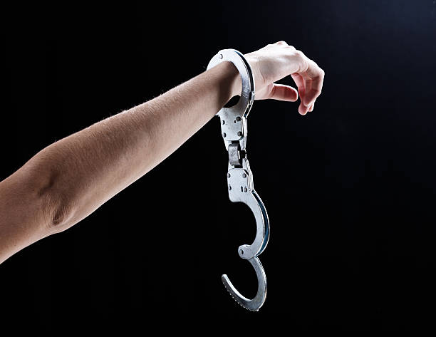 I'm free! Female hand wearing single, open handcuff. A woman's hand, holding up a hand wearing a single, open handcuff  against a black bakcground. Symbolic of release or freedom from almost anything! bail law stock pictures, royalty-free photos & images