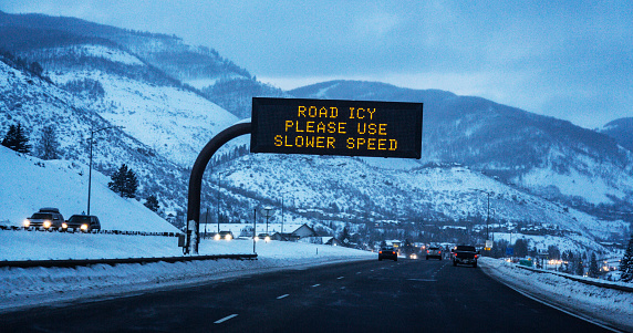 ROAD ICY - PLEASE USE SLOWER SPEED warning traffic sign. Night time first person driver view through car windshield of a digital LED light electronic road sign on US Interstate 70 near Vail, Colorado high in the Rocky Mountains Range. Winter in early February, 2016.