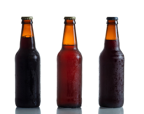Cold unopened dark and amber beer bottles on white with reflection