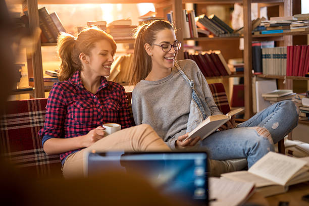 istock Happy female students relaxing while reading a book in library. 517962498