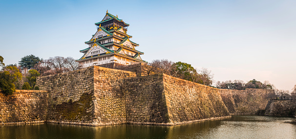 Osaka, Japan - February 26, 2016: The iconic five storey tower of Osaka Castle surrounded by the steep stone walls and tranquil moat of Osaka Castle Park in the heart of downtown Osaka, Japan's vibrant second city. Panoramic image created from six contemporaneous sequential photographs. 