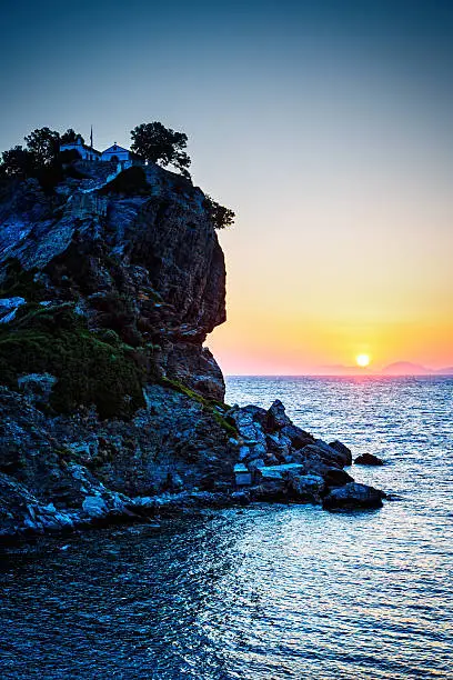 Rock with famous church Agios Ioannis Kastri on Skopelos island, Greece at sunrise, where scenes of 'Mamma Mia!' movie were filmed. Sun raises above Alonissos island.
