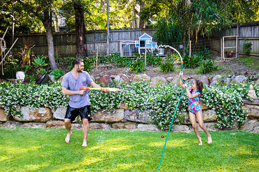 Aboriginal daughter and father water fighting in the garden.