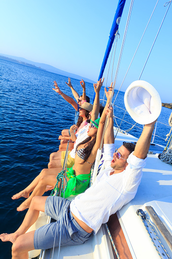 Friends having fun on sailboat, hands up, enjoying the sea travel.