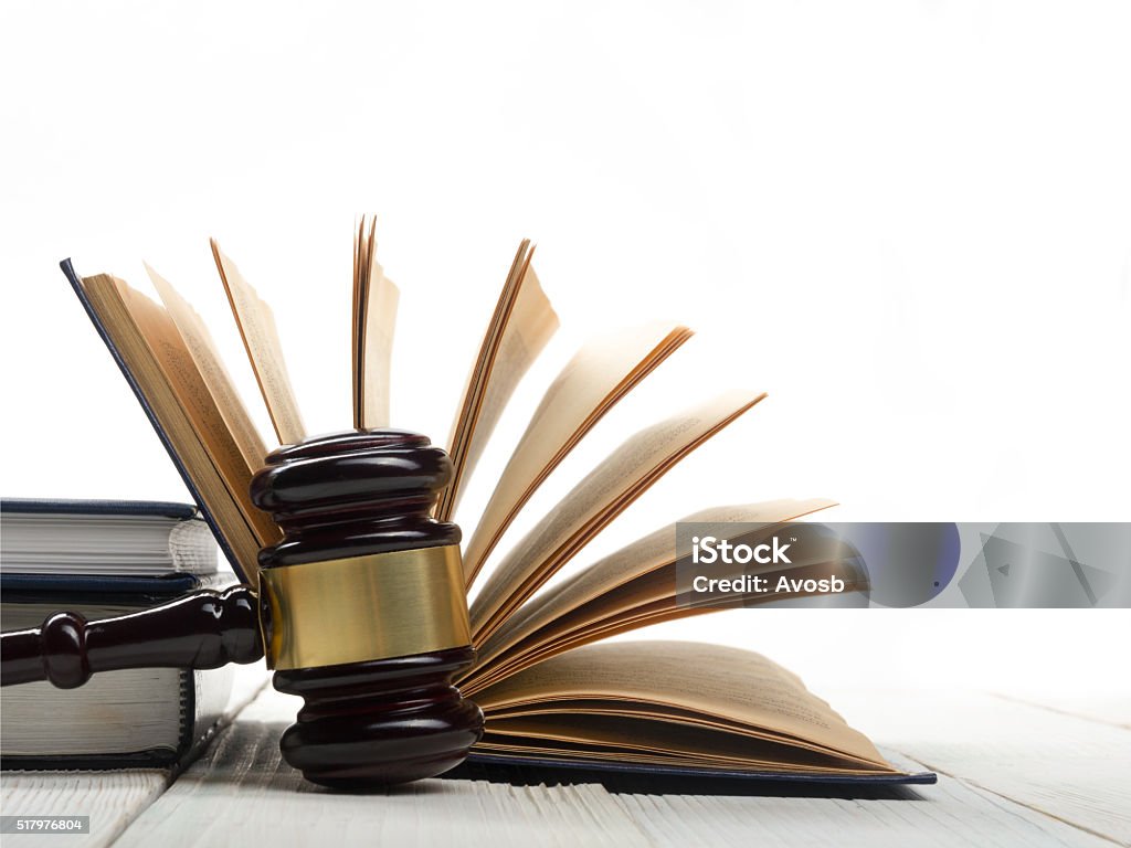 Open law book with wooden judges gavel on table in Law concept - Open law book with a wooden judges gavel on table in a courtroom or law enforcement office isolated on white background. Copy space for text. Book Stock Photo