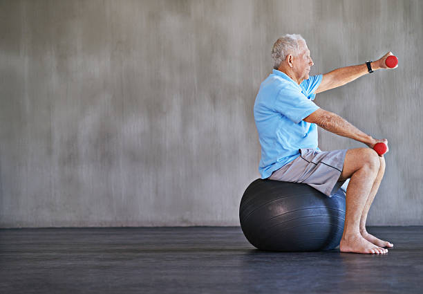 Combat aging one kilo at a time Shot of an elderly man using weights while sitting on a swiss ball fitness ball stock pictures, royalty-free photos & images