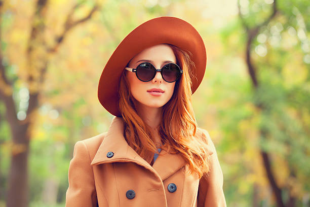 Redhead girl in sunglasses and hat in the autumn park. stock photo