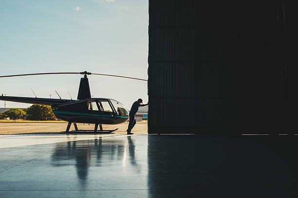 Pilot opening the helicopter hangar door. Mechanic pushing the door of a hangar with a helicopter. Pilot opening the helicopter hangar door. airplane hangar stock pictures, royalty-free photos & images