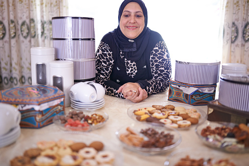 Shot of a mature muslim woman sitting in front of a variety of sweet cakes