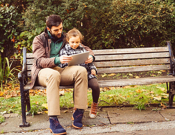 istock Father And Daughter Using Tablet Sitting On A Bench 517999025