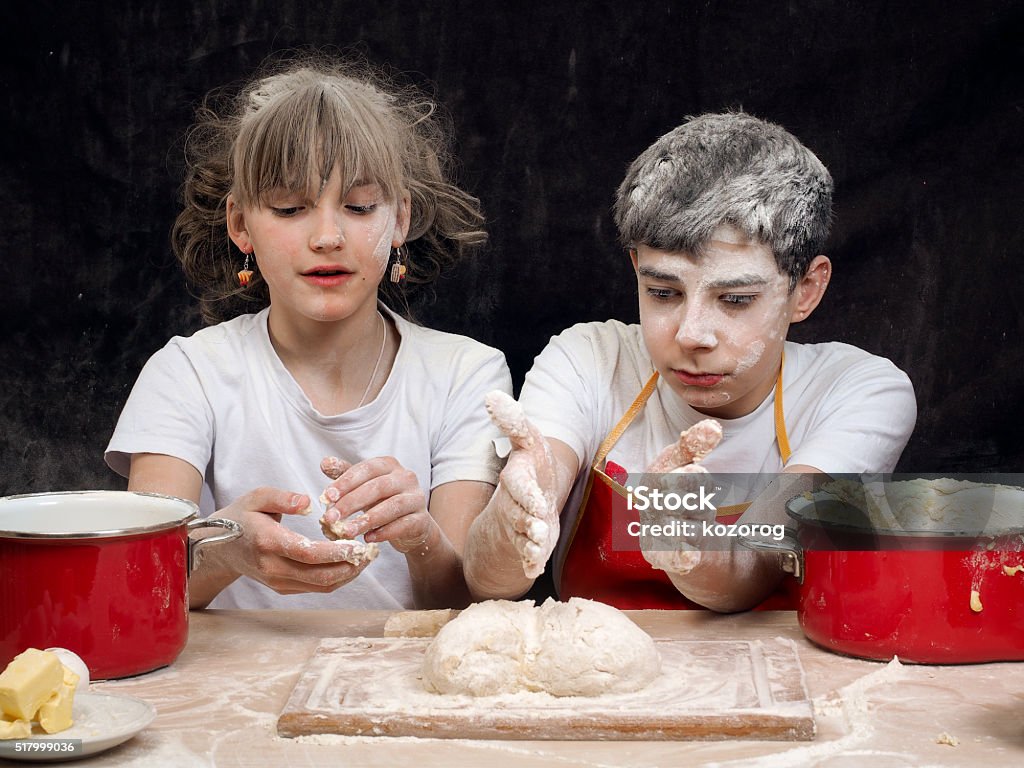 Teens knead the dough Teens knead the dough. Funny girl and the guy, mired in the flour. Baking Products. Cookware. Emotions, funny face. Relationship teens - friendship, love Adolescence Stock Photo