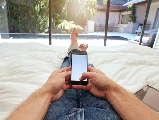 hombre relajante en la cama usando teléfono móvil - working bed smart phone bedroom fotografías e imágenes de stock