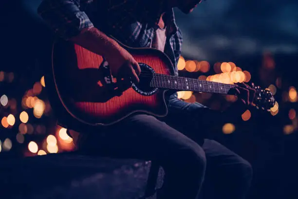 Photo of Hipster guitarist playing on a rooftop at night