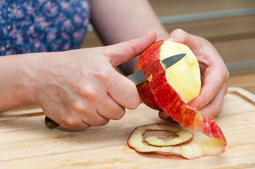 Hands peeling a cooking apple on a wooden board