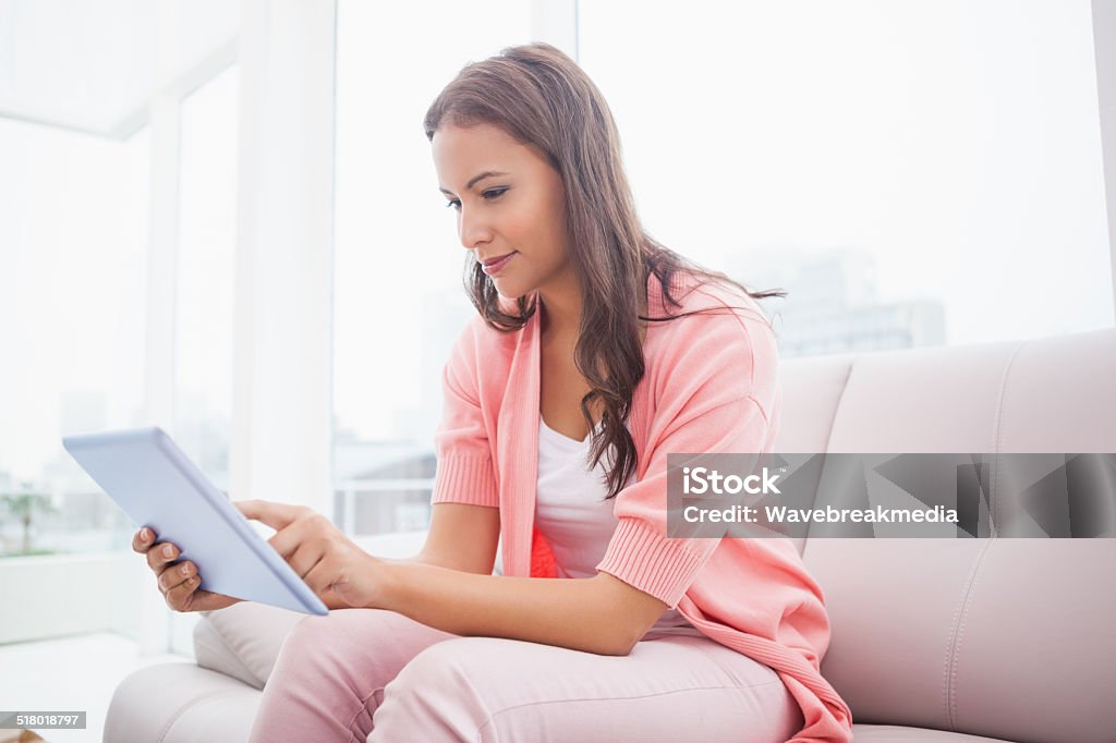 Pretty brunette using her tablet pc on the couch Pretty brunette using her tablet pc on the couch at home in the living room 20-29 Years Stock Photo