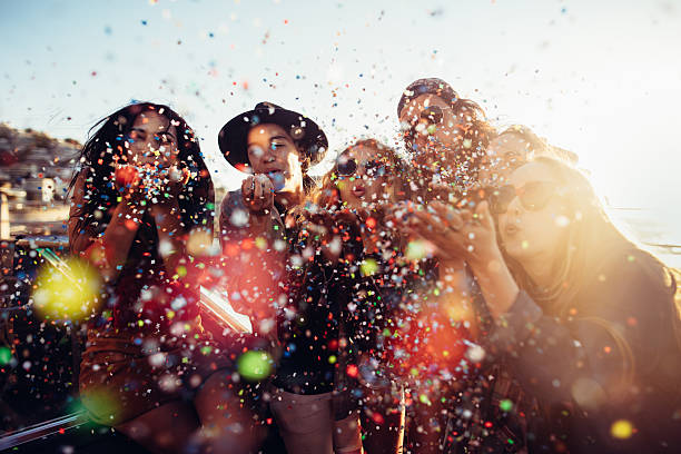 Teenager hipster friends celebrating by blowing colorful confetti from hands Group of teenager hipster friends celebrating by blowing colorful confetti from hands with sunset sun flare beach party stock pictures, royalty-free photos & images
