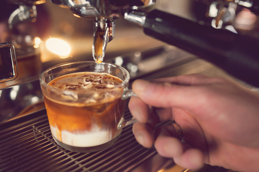 Close-up shot of a male barista hands making iced caramel macchiato coffee.