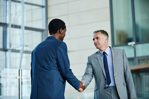 Shot of of two businessmen shaking hands in the lobby of an office building
