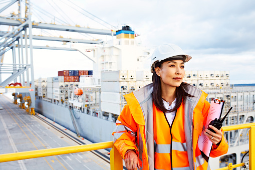 Shot of a woman in workwear standing on a commercial dock holding a walkie talkie