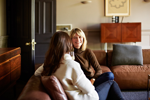 Shot of two women sitting on a sofa drinking wine and talking