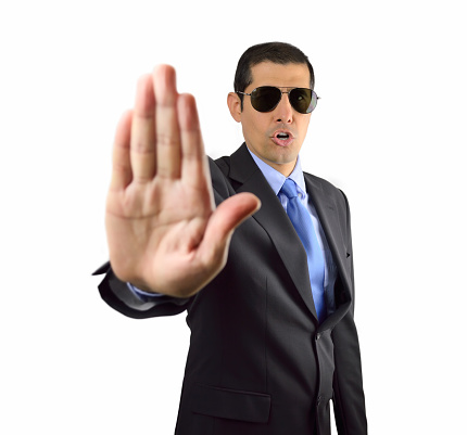 Secret service agent standing on black background and giving the halt with his hand gesturing to stop on white background