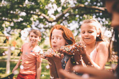 Group of children in a park on a sunny summer day blowing handfuls of colourful confetti at a party