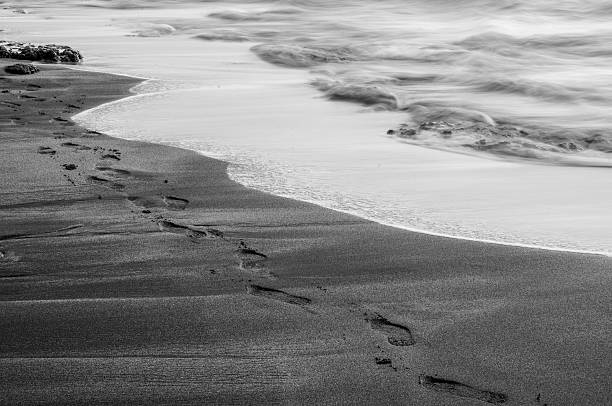 A black and white image of footprints in the sand on a beach in Hawaii.