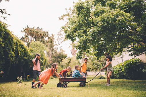 Group of children playing in a park together with some sitting in a red wagon with other friends pushing and pulling