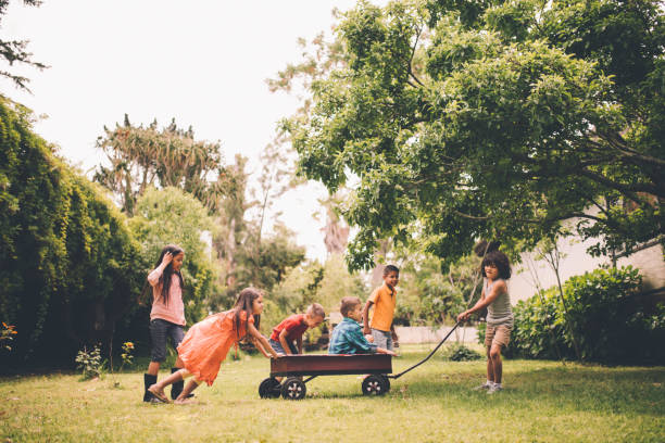 crianças levantando e puxando amigos em vermelho carroça do parque - carrinho de criança - fotografias e filmes do acervo