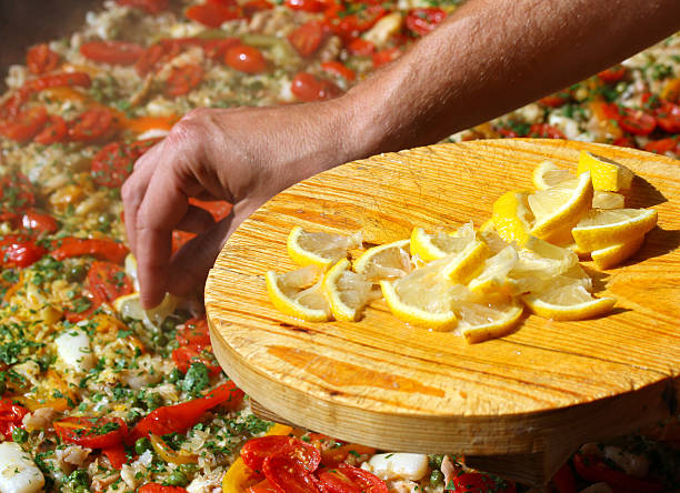 Cook puts lemon slices in the paella