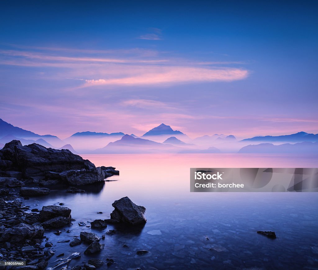 Sunset On a Rocky Beach Tranquil landscape at sunset with sea and mountains in the distance. Mountain Stock Photo